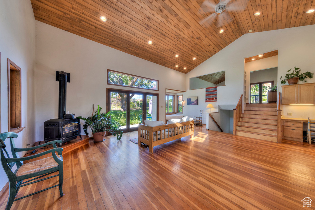 Living room featuring high vaulted ceiling, a wood stove, wood ceiling, hardwood / wood-style flooring, and stairway
