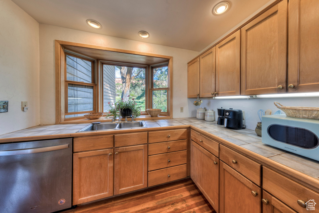 Kitchen with dishwasher, tile counters, a sink, wood finished floors, and recessed lighting