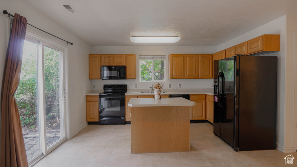 Kitchen featuring black appliances, a center island, sink, and a healthy amount of sunlight