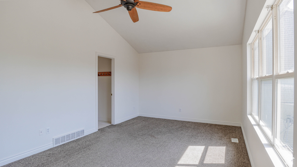 Carpeted empty room featuring high vaulted ceiling, ceiling fan, and a healthy amount of sunlight