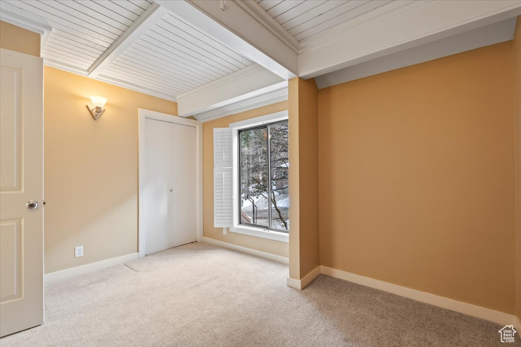 Carpeted empty room with ornamental molding, beamed ceiling, and baseboards