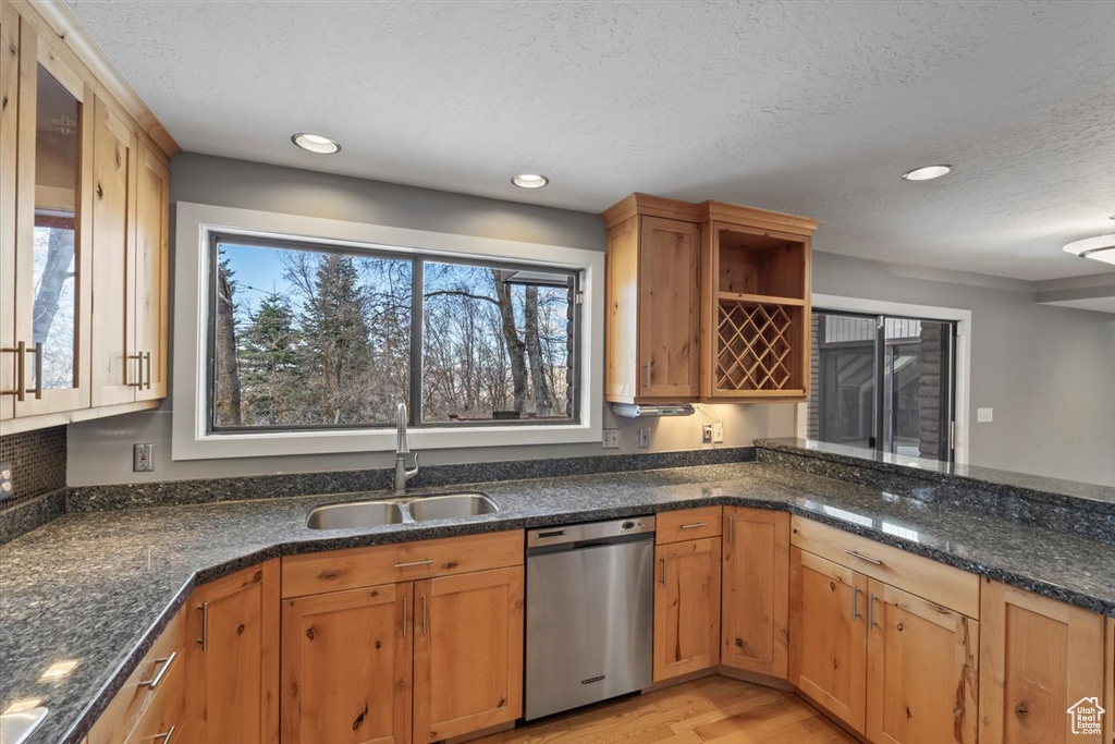 Kitchen featuring dark stone counters, stainless steel dishwasher, a textured ceiling, light wood-style floors, and a sink