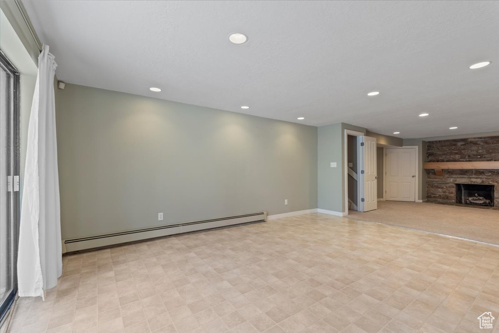 Unfurnished living room featuring a stone fireplace, a baseboard radiator, recessed lighting, baseboards, and light floors