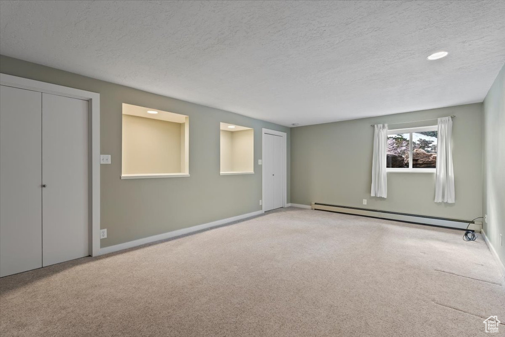 Carpeted empty room featuring a baseboard radiator, baseboards, and a textured ceiling