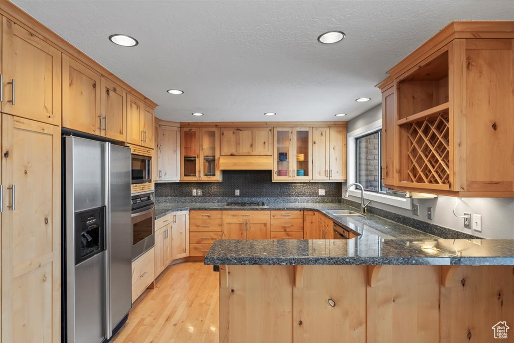 Kitchen with open shelves, stainless steel appliances, glass insert cabinets, a sink, and a peninsula