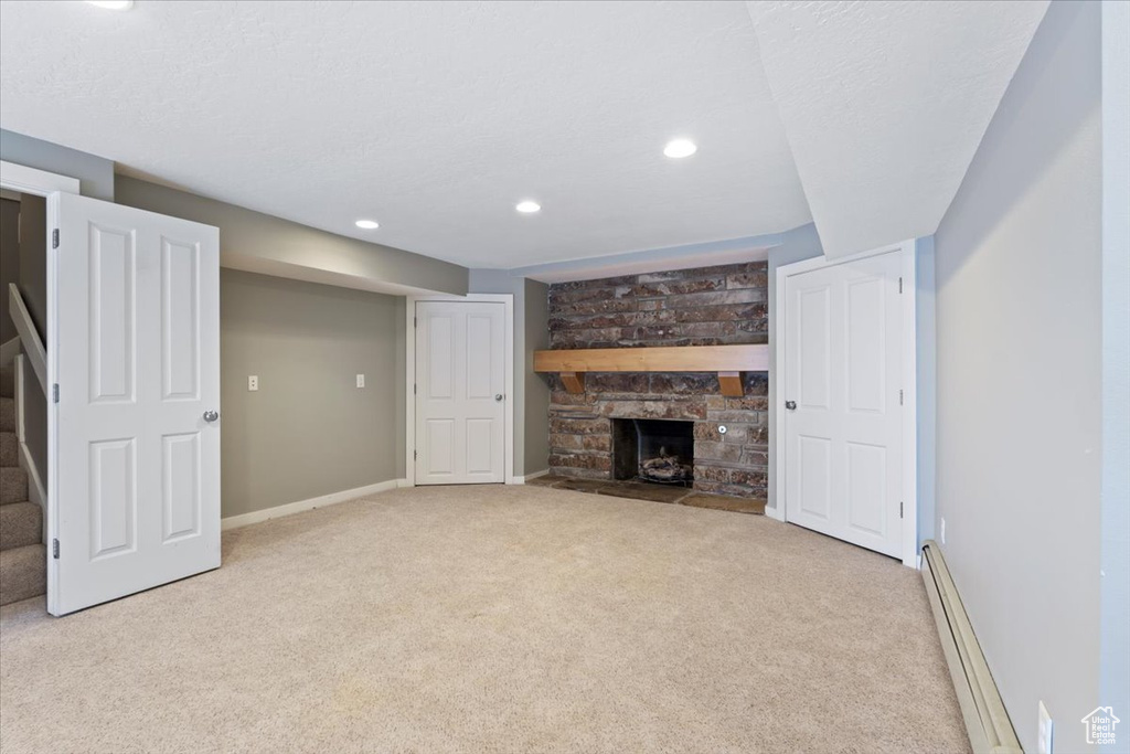 Unfurnished living room featuring baseboards, stairway, carpet, a stone fireplace, and a baseboard heating unit