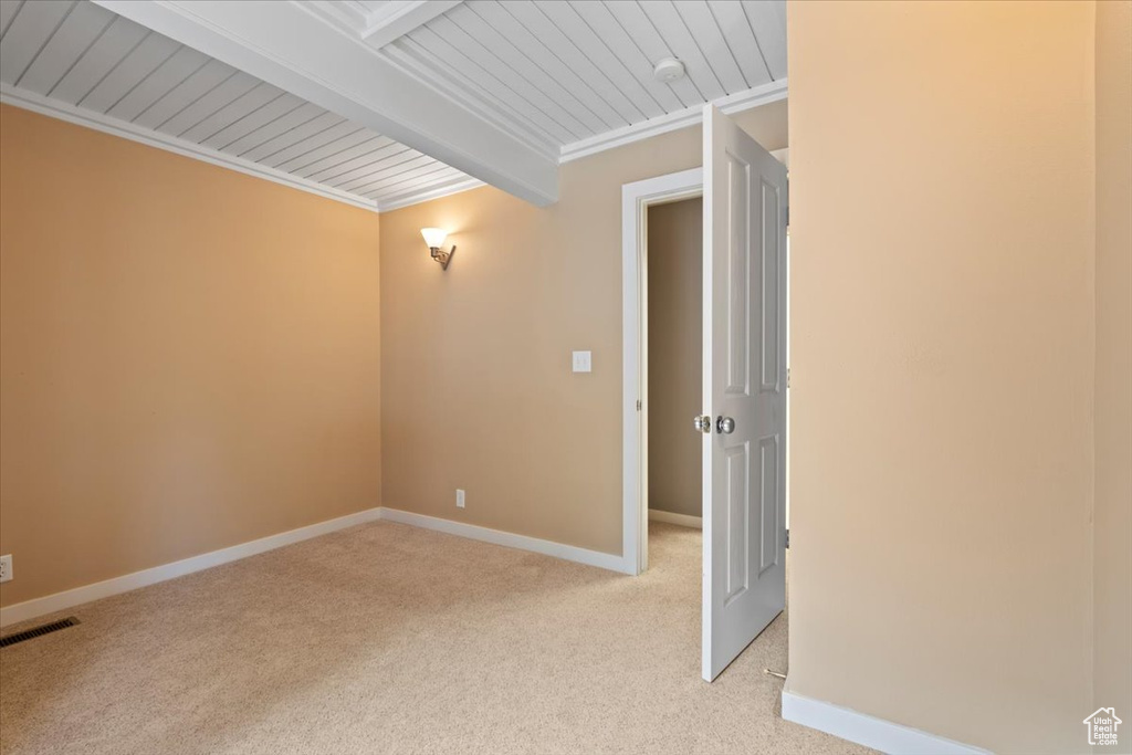 Empty room featuring light carpet, visible vents, beam ceiling, and baseboards