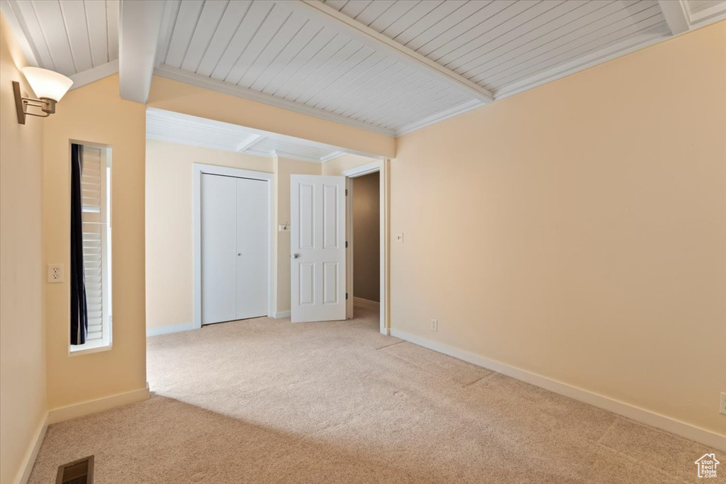 Carpeted empty room featuring ornamental molding, visible vents, lofted ceiling with beams, and baseboards