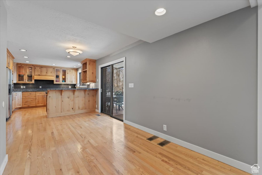 Kitchen featuring baseboards, light wood-type flooring, dark countertops, stainless steel fridge, and glass insert cabinets