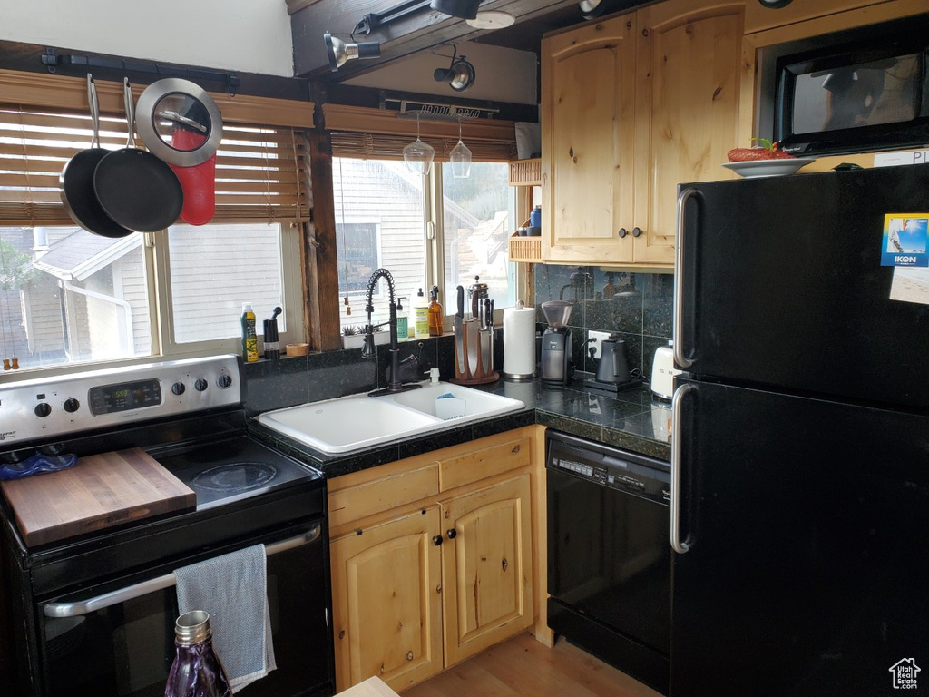 Kitchen featuring light wood-type flooring, black appliances, light brown cabinetry, sink, and decorative backsplash