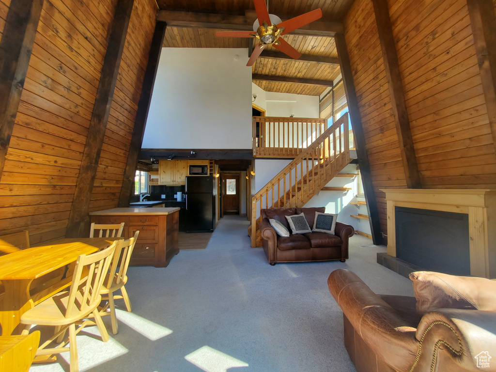 Living room with beamed ceiling, wooden ceiling, dark colored carpet, high vaulted ceiling, and ceiling fan