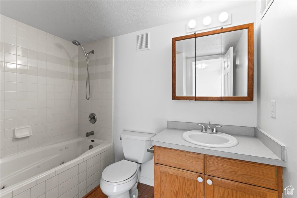 Full bathroom featuring hardwood / wood-style flooring, toilet, tiled shower / bath combo, vanity, and a textured ceiling