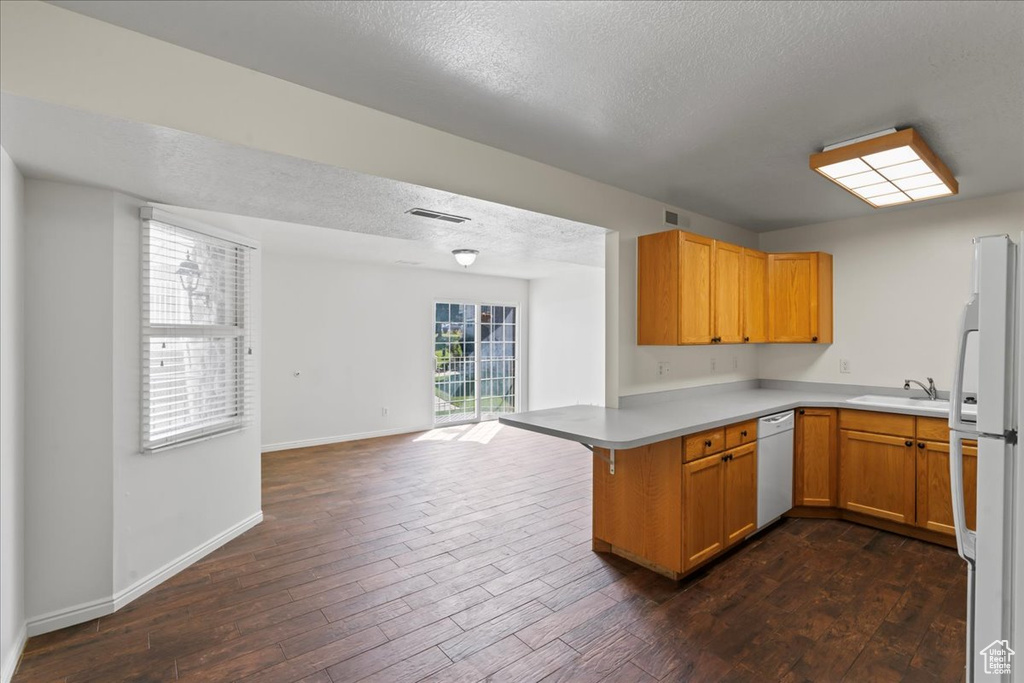 Kitchen featuring white appliances, sink, dark hardwood / wood-style floors, kitchen peninsula, and a textured ceiling