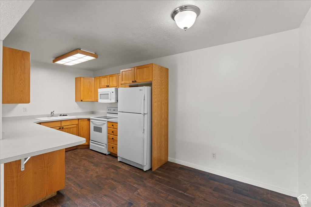 Kitchen with a textured ceiling, white appliances, dark wood-type flooring, kitchen peninsula, and sink