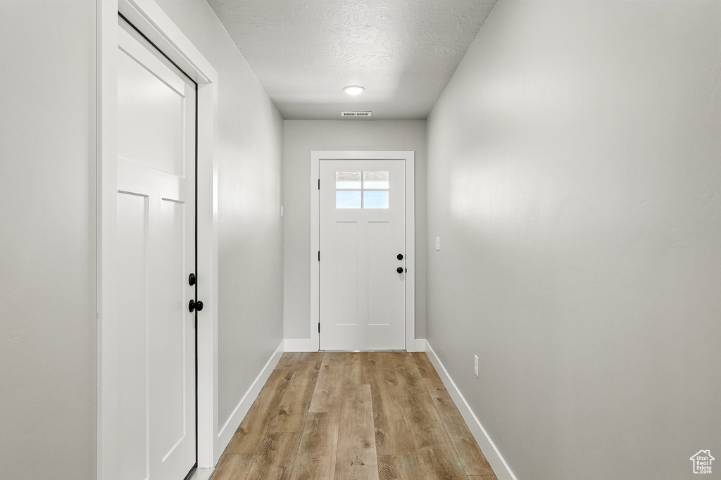 Doorway to outside with visible vents, baseboards, light wood-type flooring, and a textured ceiling