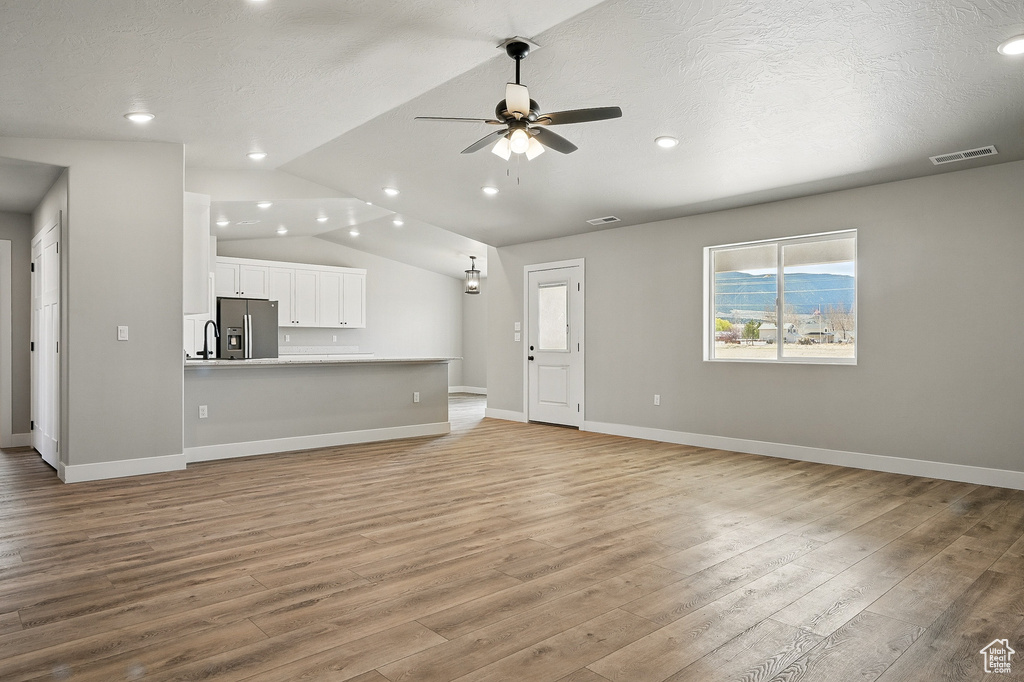 Unfurnished living room featuring visible vents, baseboards, ceiling fan, light wood finished floors, and vaulted ceiling