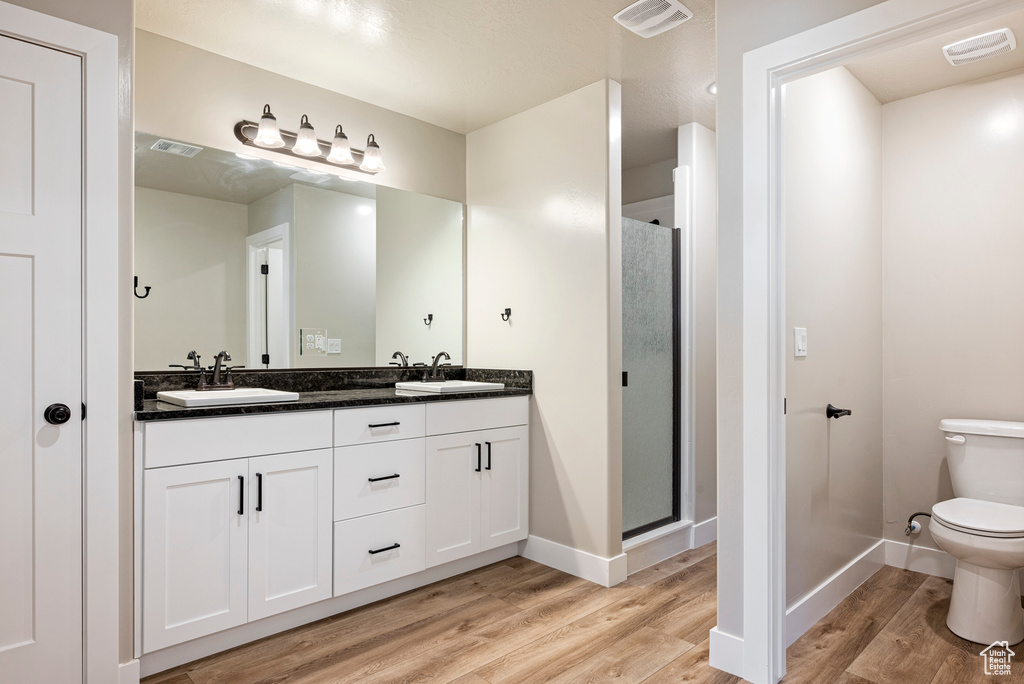 Bathroom with a shower with shower door, wood-type flooring, toilet, and vanity