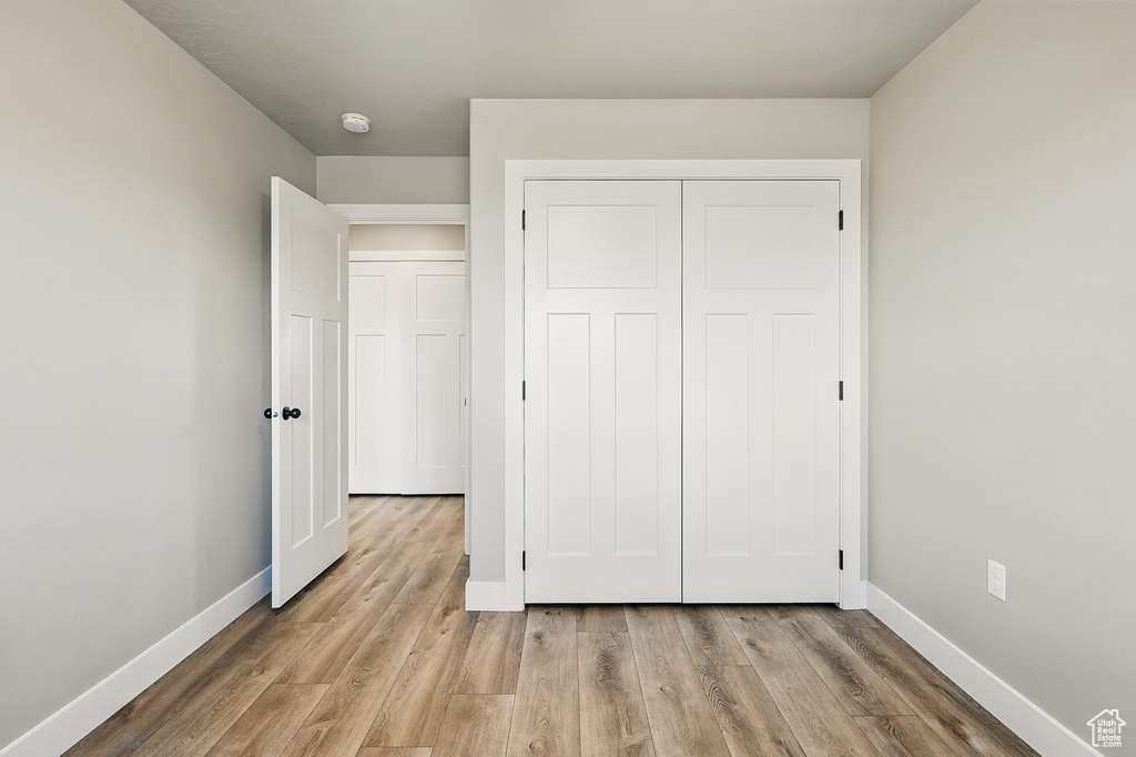 Unfurnished bedroom with light wood-style flooring, a closet, and baseboards