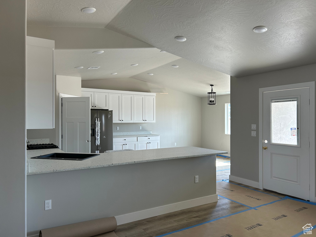 Kitchen with black fridge with ice dispenser, lofted ceiling, kitchen peninsula, hardwood / wood-style flooring, and white cabinetry