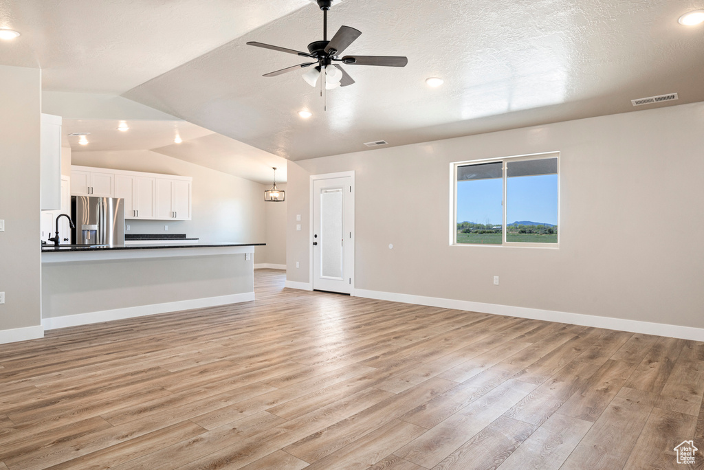 Unfurnished living room with light hardwood / wood-style flooring, sink, lofted ceiling, ceiling fan, and a textured ceiling