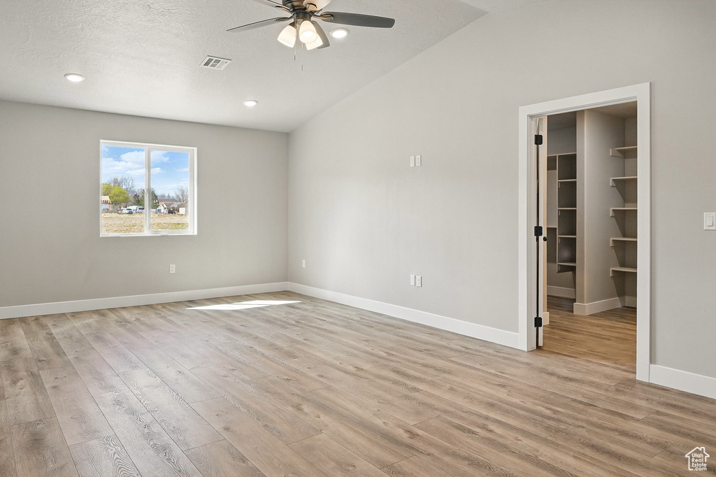 Unfurnished bedroom with baseboards, vaulted ceiling, light wood-style flooring, a walk in closet, and visible vents