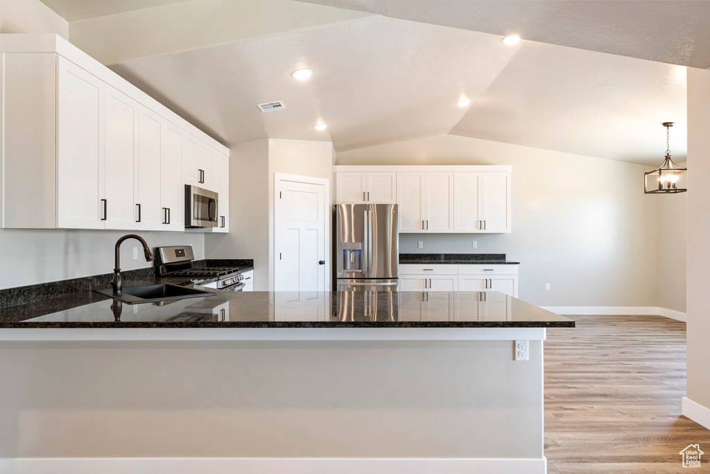 Kitchen featuring light hardwood / wood-style flooring, stainless steel appliances, decorative light fixtures, kitchen peninsula, and vaulted ceiling