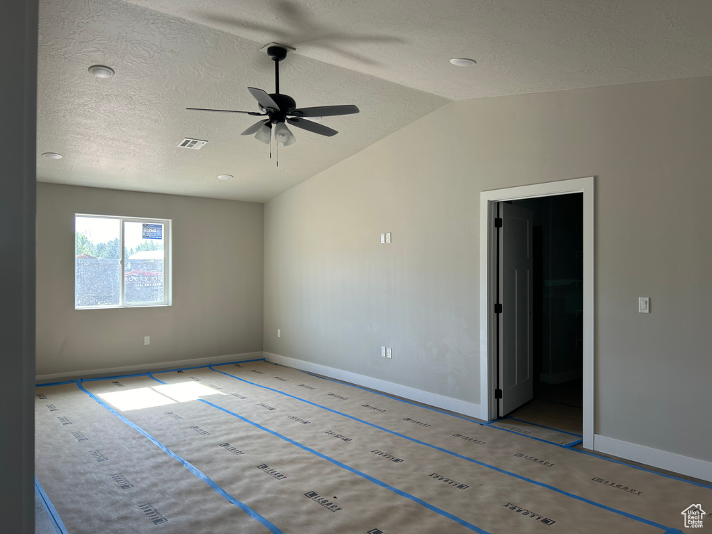 Empty room featuring lofted ceiling, ceiling fan, and a textured ceiling