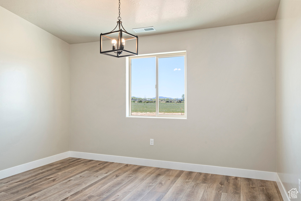 Empty room featuring a notable chandelier and wood-type flooring