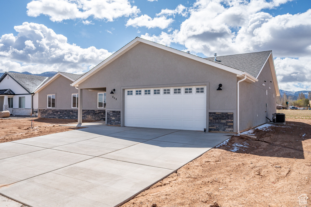 View of front of house featuring an attached garage, stone siding, driveway, and stucco siding