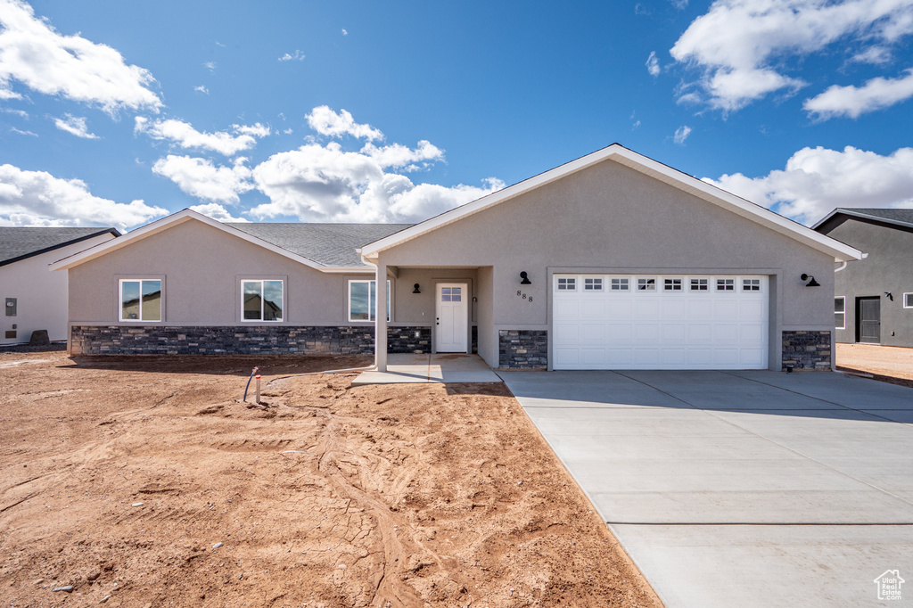 Single story home with a garage, stucco siding, stone siding, and concrete driveway