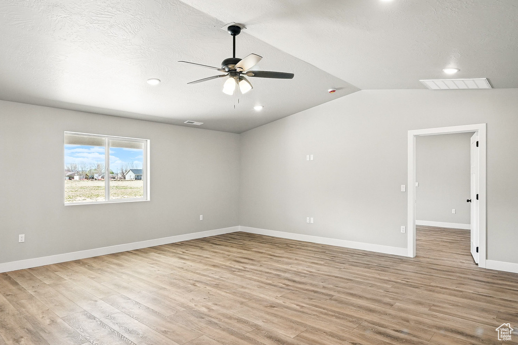 Empty room featuring ceiling fan, light wood-style flooring, visible vents, lofted ceiling, and baseboards