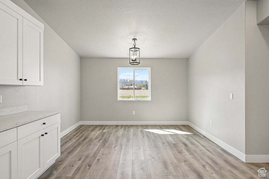 Unfurnished dining area with baseboards, light wood-style floors, and a textured ceiling