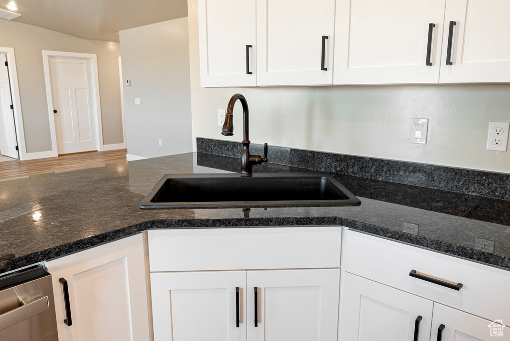 Kitchen featuring wood-type flooring, stainless steel dishwasher, sink, dark stone countertops, and white cabinets