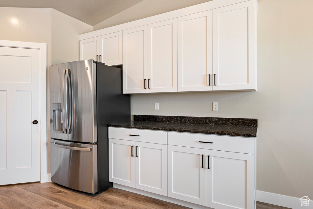 Kitchen featuring dark stone counters, stainless steel fridge, light hardwood / wood-style flooring, and white cabinets