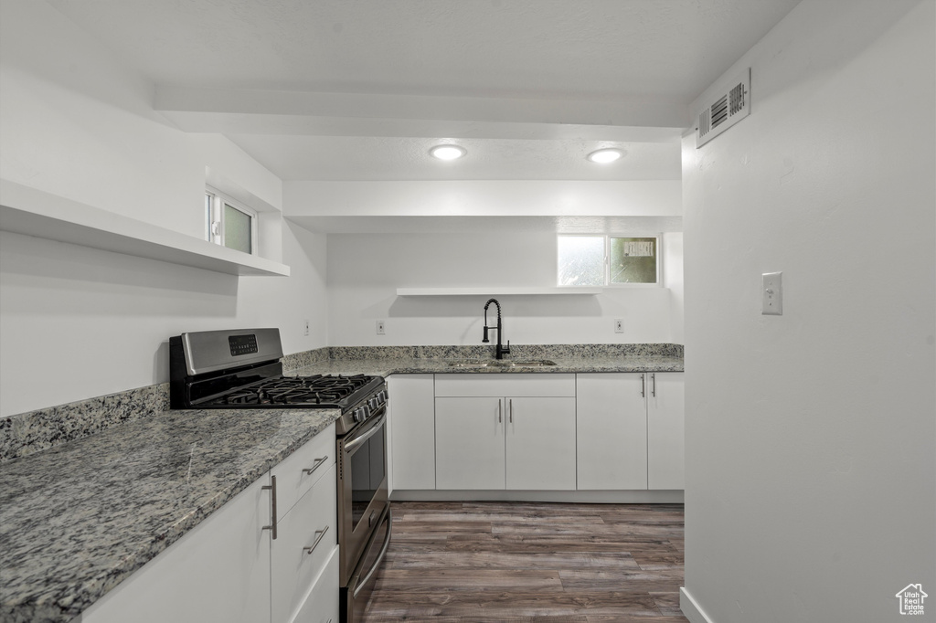 Kitchen with white cabinetry, gas range, sink, and light stone countertops