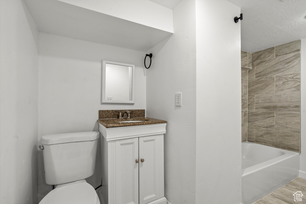 Full bathroom with tiled shower / bath, hardwood / wood-style floors, toilet, vanity, and a textured ceiling