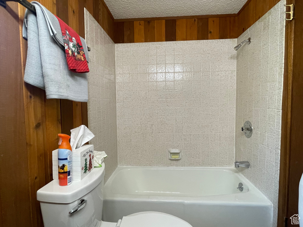 Bathroom with wood walls, toilet, and tiled shower / bath combo