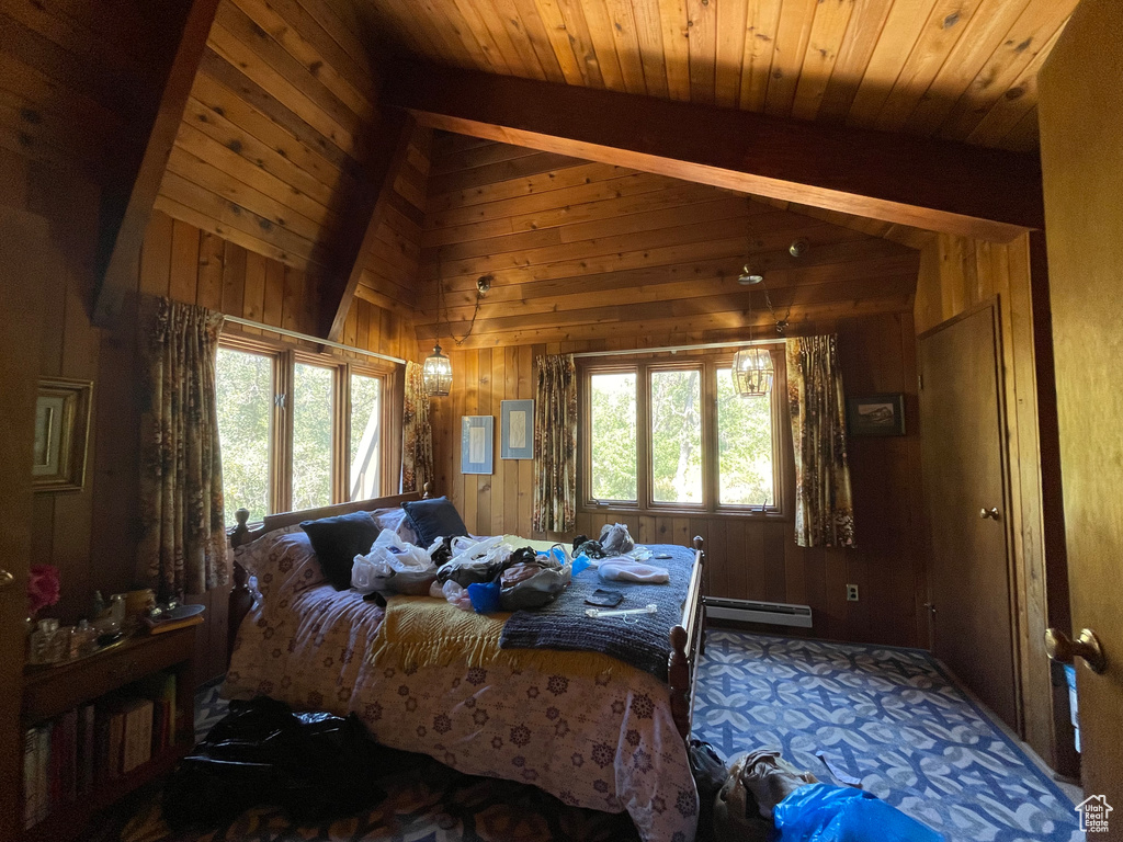 Bedroom with baseboard heating, wooden walls, and multiple windows