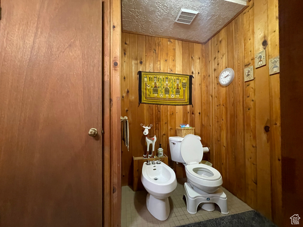 Bathroom with tile patterned floors, toilet, a bidet, wood walls, and a textured ceiling