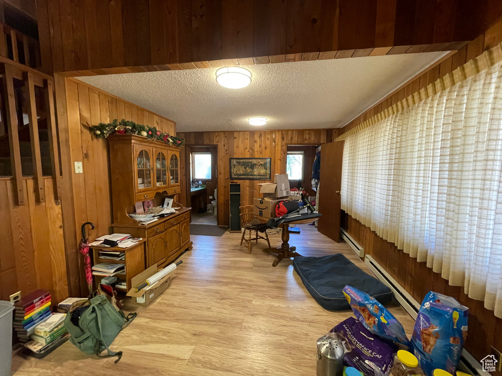 Interior space with a baseboard heating unit, a textured ceiling, wooden walls, and light hardwood / wood-style floors