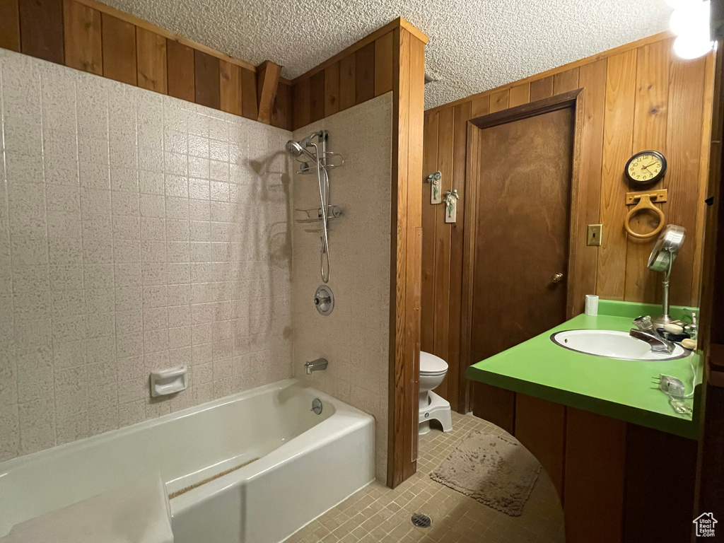 Full bathroom featuring a textured ceiling, vanity, wood walls, toilet, and tiled shower / bath combo