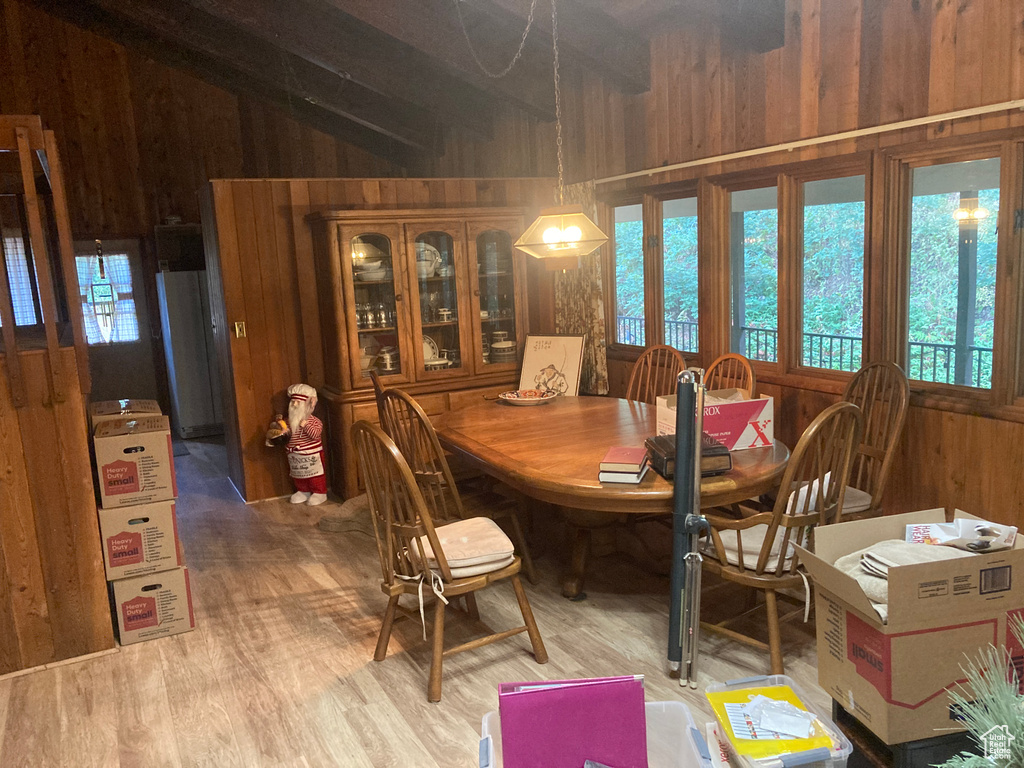 Dining room with wood-type flooring, vaulted ceiling with beams, and wooden walls