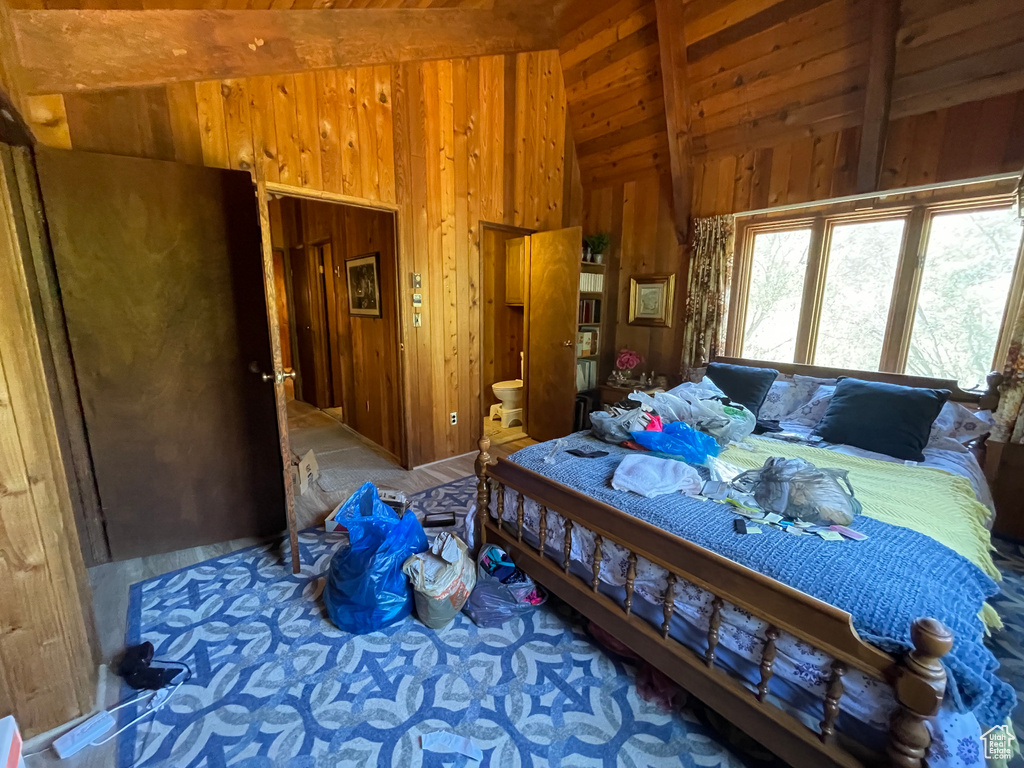 Bedroom featuring ensuite bath, lofted ceiling with beams, and wood walls