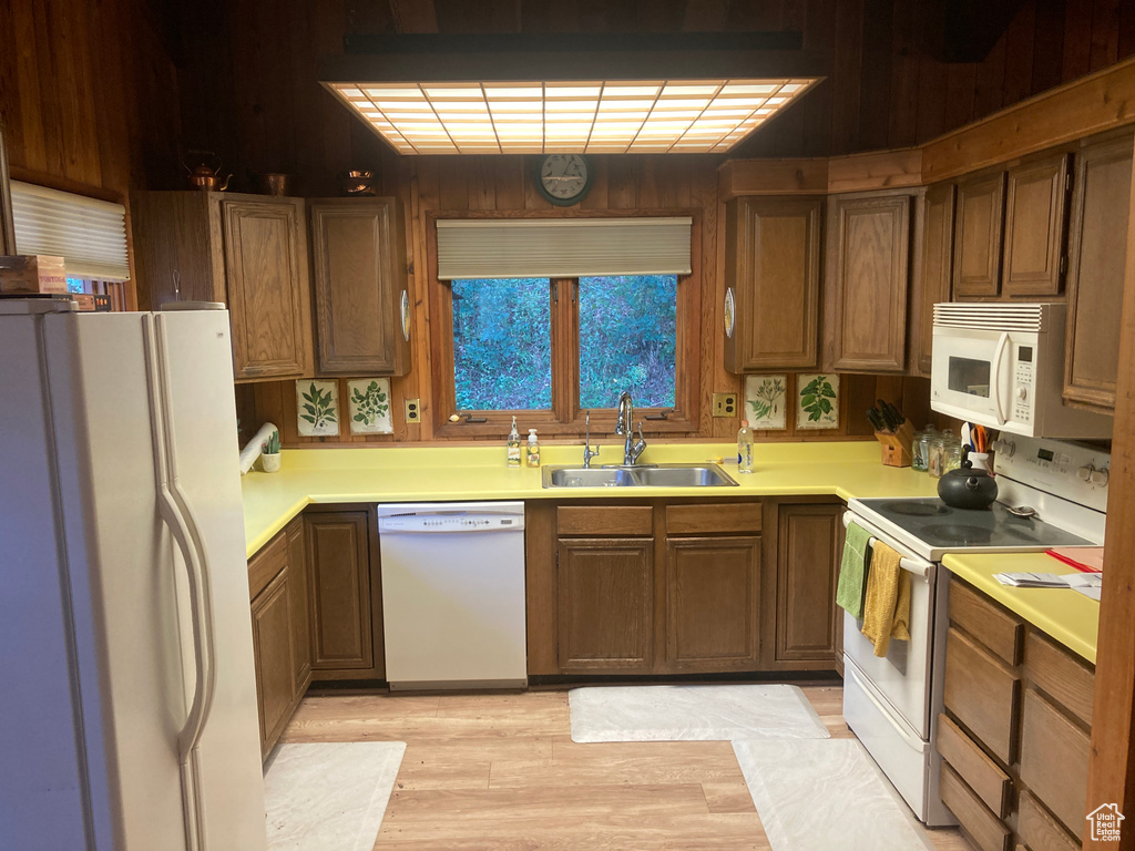 Kitchen with white appliances, light hardwood / wood-style flooring, sink, and wooden walls