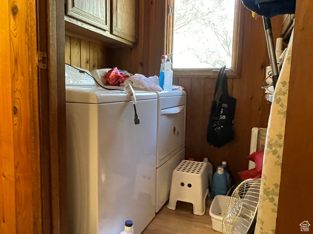 Laundry room with cabinets, washer and clothes dryer, light wood-type flooring, and wooden walls