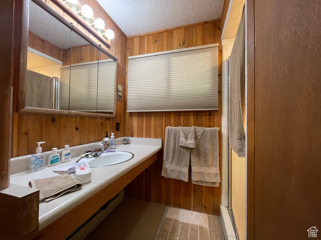 Bathroom with tile patterned flooring, wooden walls, sink, and a shower with shower door