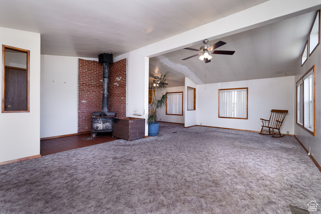 Unfurnished living room with vaulted ceiling, dark colored carpet, ceiling fan, and a wood stove
