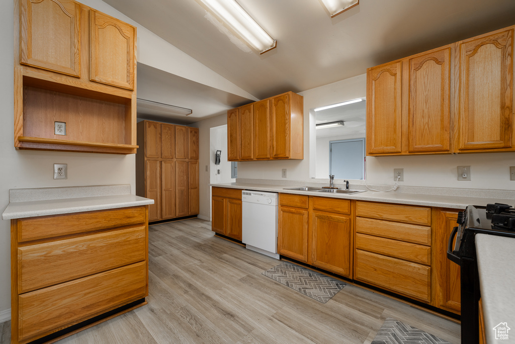 Kitchen with light wood-type flooring, stove, white dishwasher, sink, and vaulted ceiling