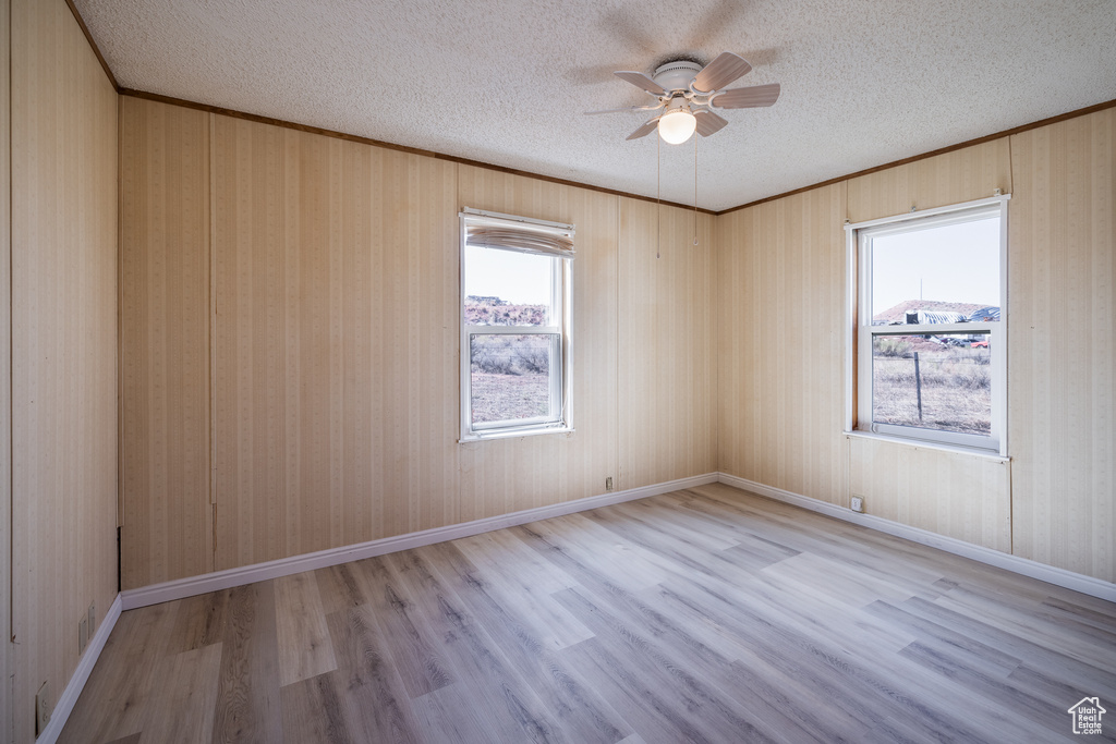 Unfurnished room featuring a textured ceiling, wood walls, ceiling fan, and light hardwood / wood-style floors