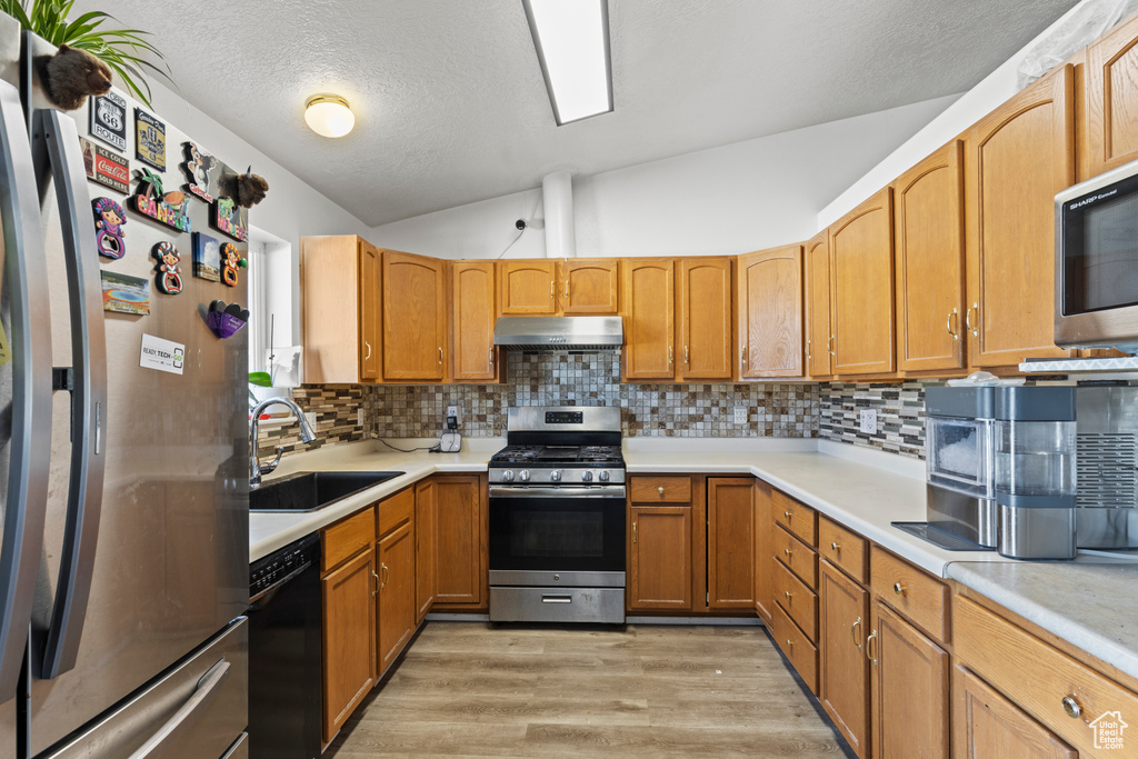 Kitchen featuring light hardwood / wood-style floors, stainless steel appliances, lofted ceiling, sink, and tasteful backsplash